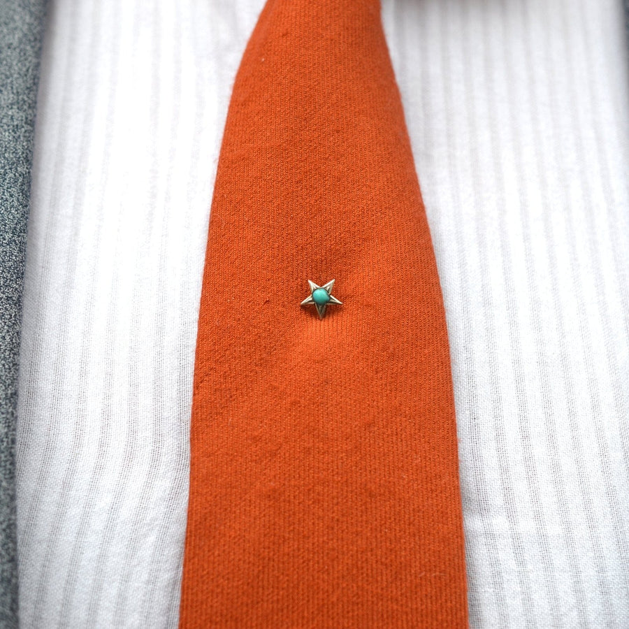 Victorian silver and turquoise star tie pin accentuating an orange tie, symbolizing love and remembrance.