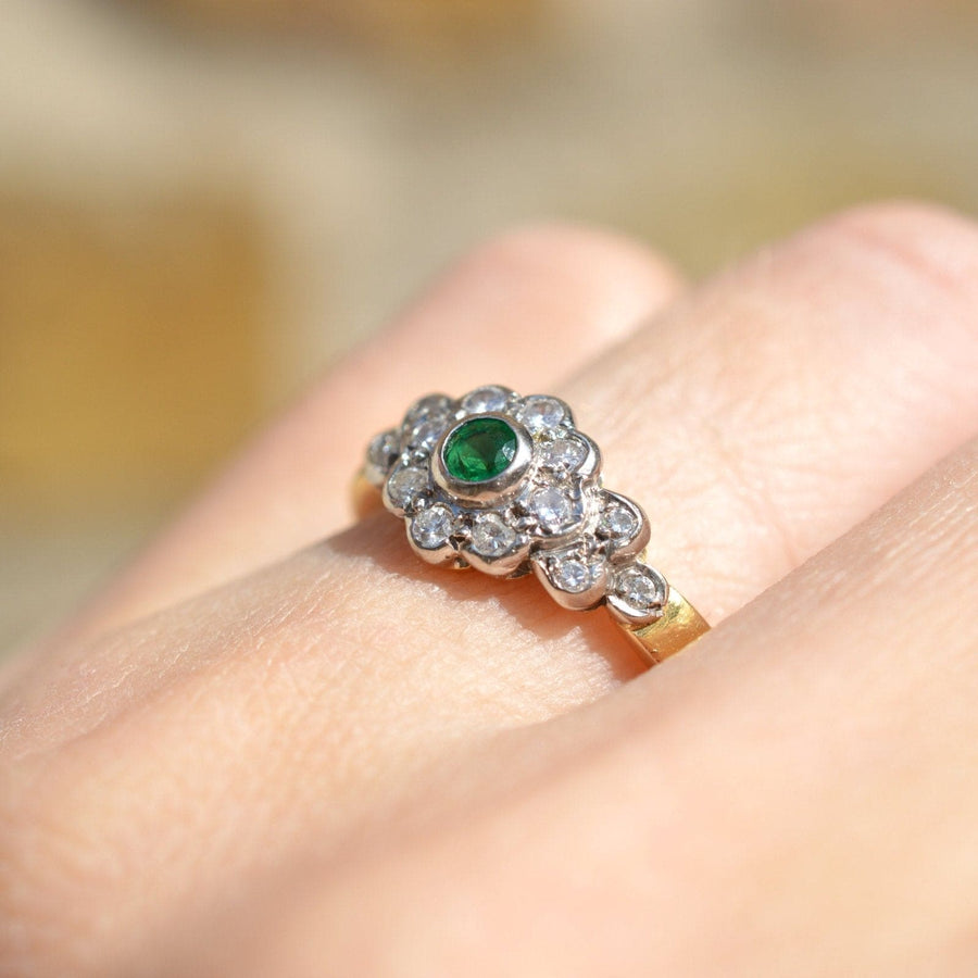 Vintage 18ct gold emerald and diamond cluster ring worn on a hand, showcasing the green emerald and sparkling diamonds.