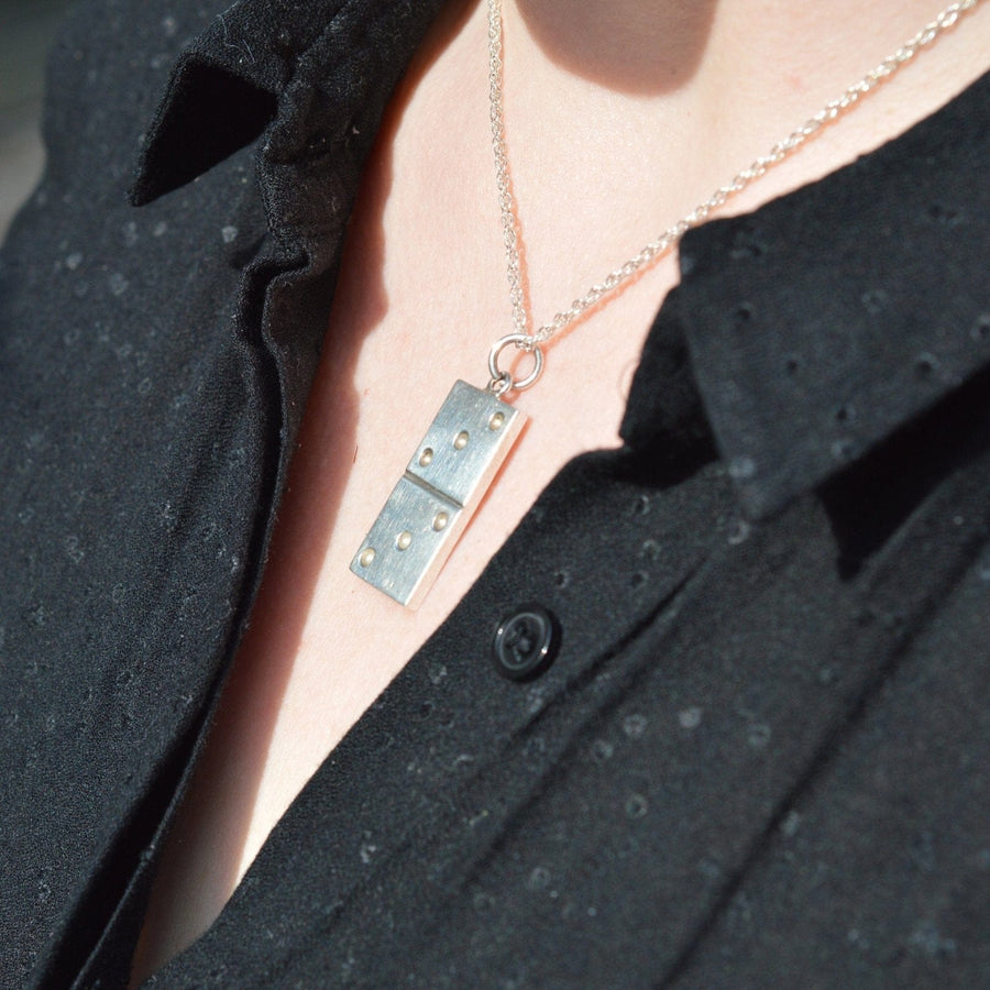 Vintage 1970s large silver domino pendant worn on a person's neck against a black shirt.