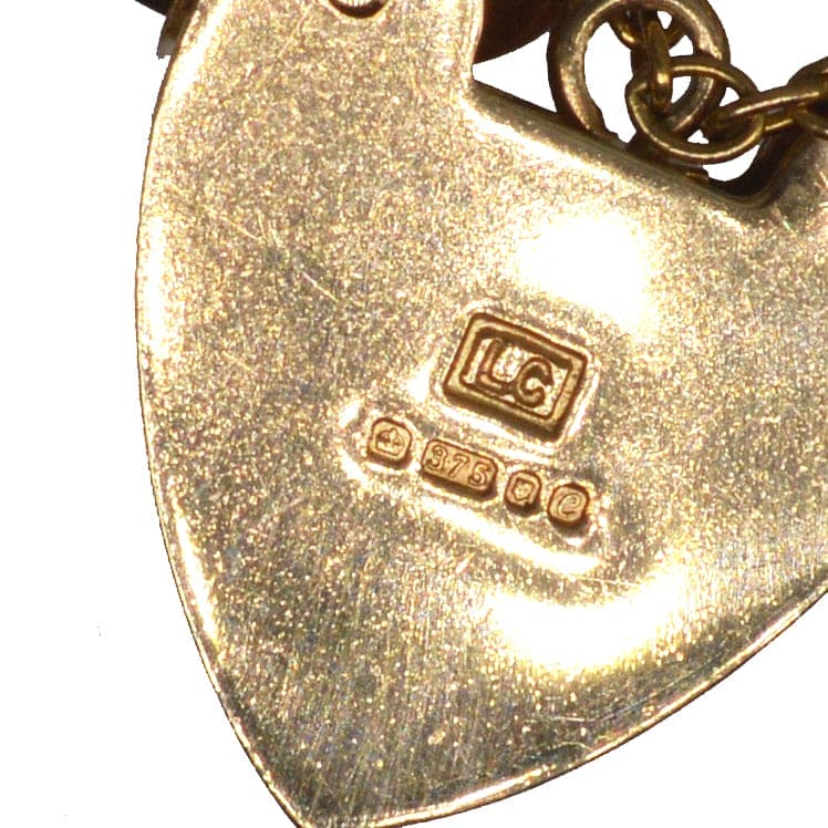Close-up of heart-shaped padlock with hallmarks indicating 9ct gold quality on a vintage bracelet.