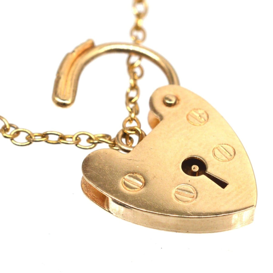 Close-up of a heart-shaped gold padlock on a chain, featuring an openable design and vintage finish.