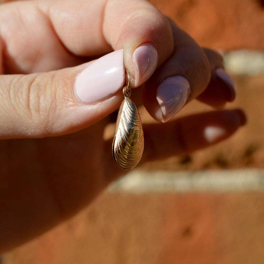 Vintage 9ct gold mussel shell charm pendant held between fingers against a blurred brick background.