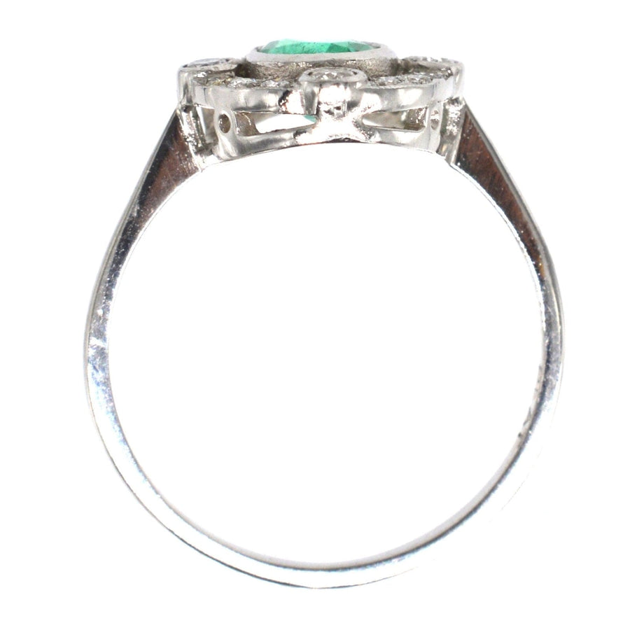 Vintage platinum ring featuring an oval emerald center, surrounded by diamond clusters. Elegant engagement ring.