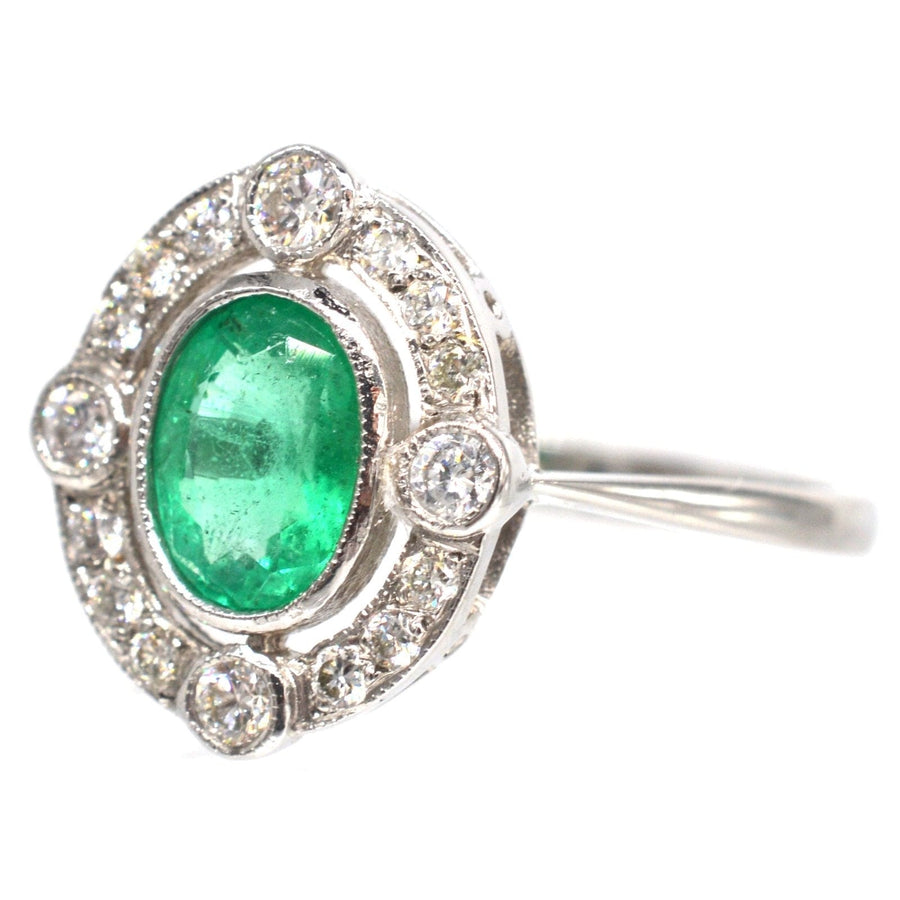 Elegant vintage platinum ring featuring a vibrant oval emerald surrounded by diamond clusters.