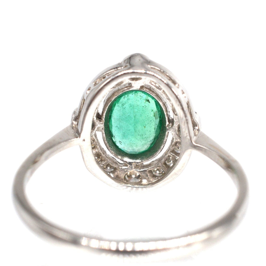Vintage platinum emerald ring featuring an oval emerald center surrounded by a diamond cluster, perfect for an engagement.