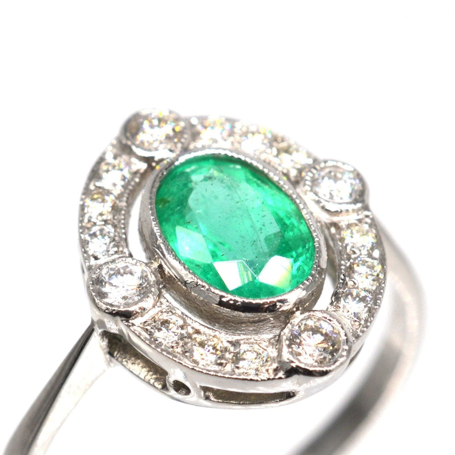 Elegant vintage platinum ring featuring an oval emerald surrounded by diamond clusters, perfect for an engagement.