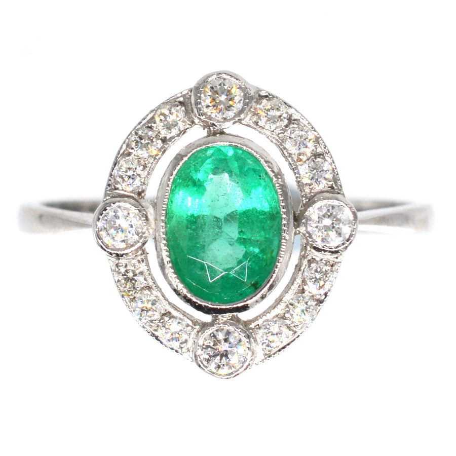 Vintage platinum emerald and diamond cluster ring featuring an oval emerald surrounded by sparkling diamonds.