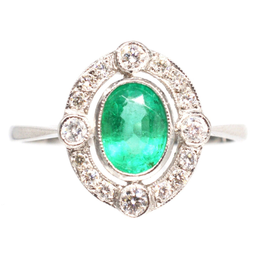 Vintage platinum ring featuring a vibrant oval emerald surrounded by diamond clusters, ideal for an elegant engagement ring.