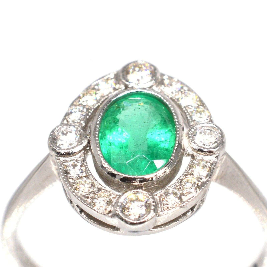 Vintage platinum ring featuring a vibrant oval emerald surrounded by diamond clusters, perfect for an elegant engagement.