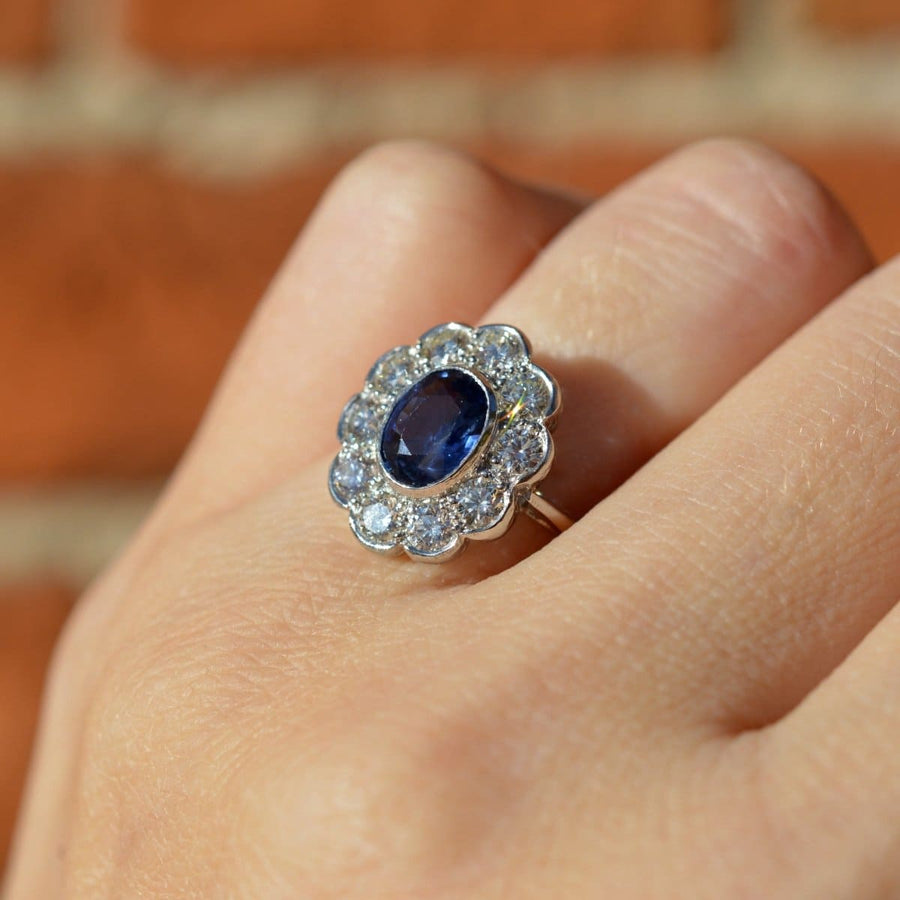 Vintage platinum sapphire and diamond cluster ring featuring a 1 carat sapphire and 1.2 carats of diamonds in a scalloped setting.